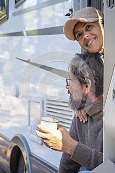 Young couple of tourists with camper motor home sitting at the door enjoing nature outdoors leisure feeling. Travel people and