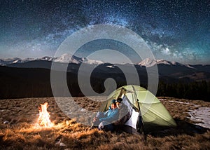 Young couple tourists having a rest in the camping at night under beautiful starry sky and milky way