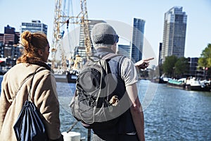 Young couple tourists looking and pointing to Rotterdam city harbour, future architecture concept, industrial lifestyle