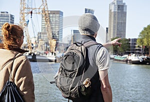 Young couple tourists looking and pointing to Rotterdam city harbour, future architecture concept, industrial lifestyle