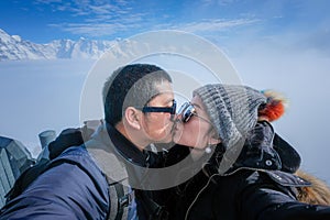 Young Couple Tourists selfie kiss with mobile phone near view of the Swiss Skyline from Schilthorn, Switzerland