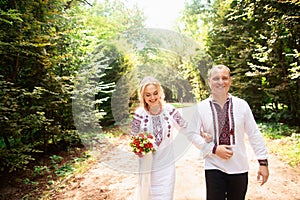 A young couple in a traditional Ukrainian clothing whith bouquet walking in the sunny park