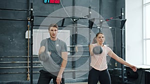 Young couple training in gym weightlifting squatting with kettlebells together