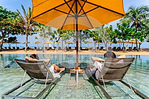 Young couple traveler relaxing and enjoying the beach view by a tropical beachfront resort pool while traveling for summer