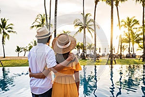 Young couple traveler relaxing and enjoying the sunset by a tropical resort pool while traveling for summer vacation