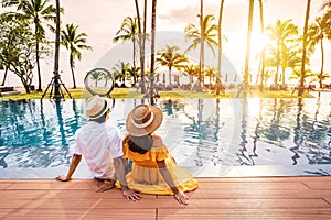 Young couple traveler relaxing and enjoying the sunset by a tropical resort pool while traveling for vacation