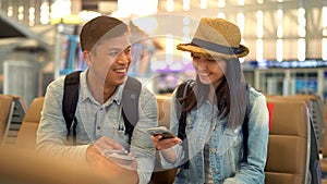 Young  Couple traveler sitting and relax in the terminal aiith suitcase standing on the moving walkway while using smartphone.