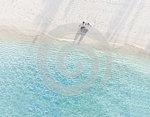 Young couple traveler sitting and relaxing at beautiful tropical white sand beach with wave foam and transparent sea, Summer