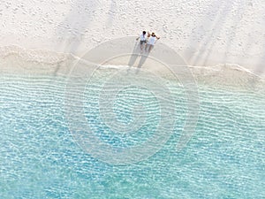 Young couple traveler sitting and relaxing at beautiful tropical white sand beach with wave foam and transparent sea