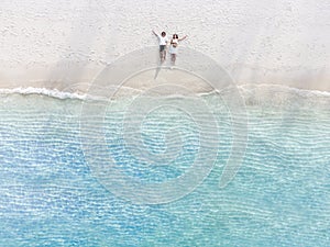 Young couple traveler sitting and relaxing at beautiful tropical white sand beach with wave foam and transparent sea