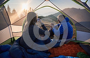 Young couple travelers drinking coffee during camping trip in mountains.