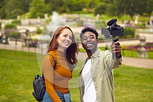 Young Couple Travelling Through City Park Together Vlogging To Video Camera On Handheld Tripod photo