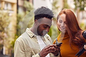 Young Couple Travelling Through City Together Vlogging With Camera Looking At Mobile Phone photo