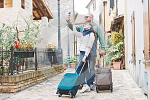 A young couple travelling with luggage and walking in an old italian town