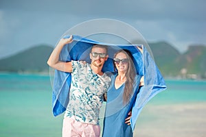 Young couple at tropical beach under the towel hiding from tropical rain.