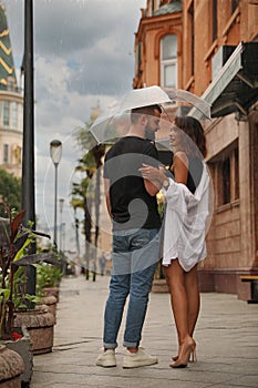 Young couple with umbrella enjoying time together under rain on city street