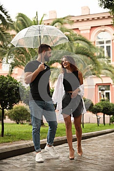 Young couple with umbrella enjoying time together under rain on city street