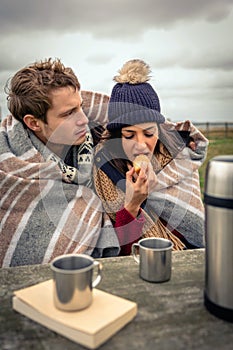 Young couple under blanket eating muffin outdoors in a cold day