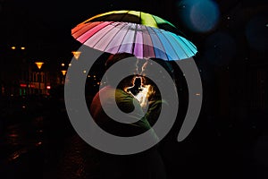 Young couple under an umbrella kisses at night on a city street.