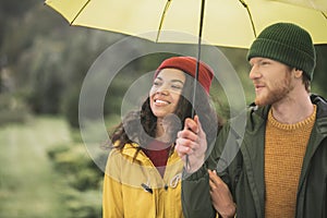 Young couple under yellow umbrela looking contented