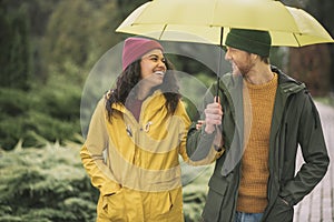 Young couple under yellow umbrela looking happy