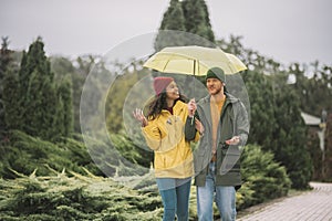 Young couple under yellow umbrela walking in the park