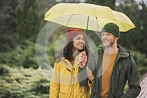 Young couple under yellow umbrela walking in the park