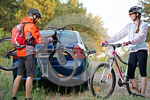 Young Couple Unmounting Mountain Bikes from Bike Rack on the Car. Adventure and Family Travel Concept.