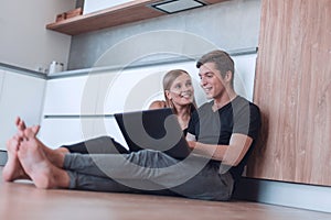 Young couple uses a laptop sitting on the floor of a new apartment