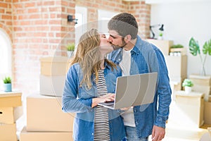 Young couple using computer laptop standing on a room around cardboard boxes, happy for moving to a new apartment