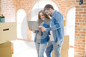 Young couple using computer laptop standing on a room around cardboard boxes, happy for moving to a new apartment