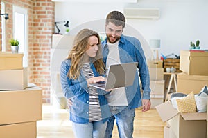 Young couple using computer laptop standing on a room around cardboard boxes, happy for moving to a new apartment