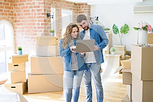 Young couple using computer laptop standing on a room around cardboard boxes, happy for moving to a new apartment