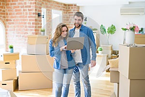 Young couple using computer laptop standing on a room around cardboard boxes, happy for moving to a new apartment