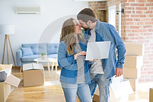 Young couple using computer laptop standing on a room around cardboard boxes, happy for moving to a new apartment