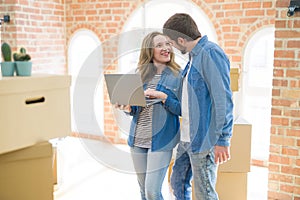 Young couple using computer laptop standing on a room around cardboard boxes, happy for moving to a new apartment