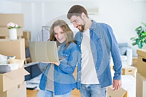 Young couple using computer laptop standing on a room around cardboard boxes, happy for moving to a new apartment