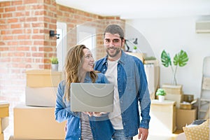 Young couple using computer laptop standing on a room around cardboard boxes, happy for moving to a new apartment