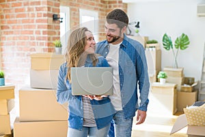 Young couple using computer laptop standing on a room around cardboard boxes, happy for moving to a new apartment