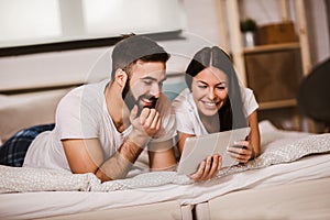 Young couple using digital tablet in bed at home