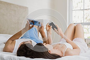 Young couple using digital tablet and mobile phone while lying on bed