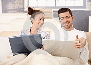 Young couple using laptop in bed at home smiling