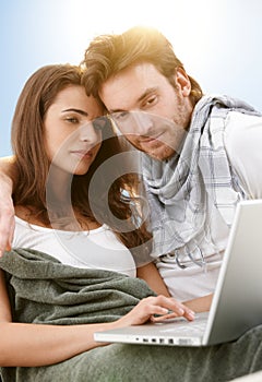 Young couple using laptop outdoor in sunlight