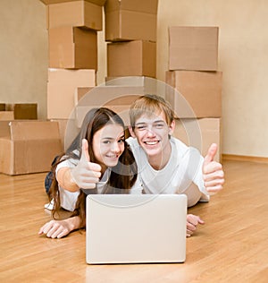 Young couple using laptop in their new home and showing thumbs up