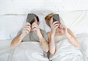 Young couple using mobile phone in bed ignoring each other in relationship communication problems