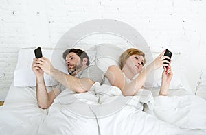 young couple using mobile phone in bed ignoring each other in relationship communication problems