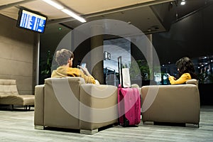 Young couple using mobile phones while waiting for the plane in the airport waiting room. Couple sitting with yellow clothes and