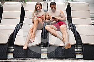 Young couple using mobile by pool