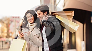 Young couple using phone after shopping in mall