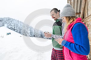 Young Couple Using Smart Phone Snowy Village Wooden Country House Man And Woman Online Messaging Winter Snow